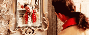 Gaston stares at himself in a mirror, lovingly