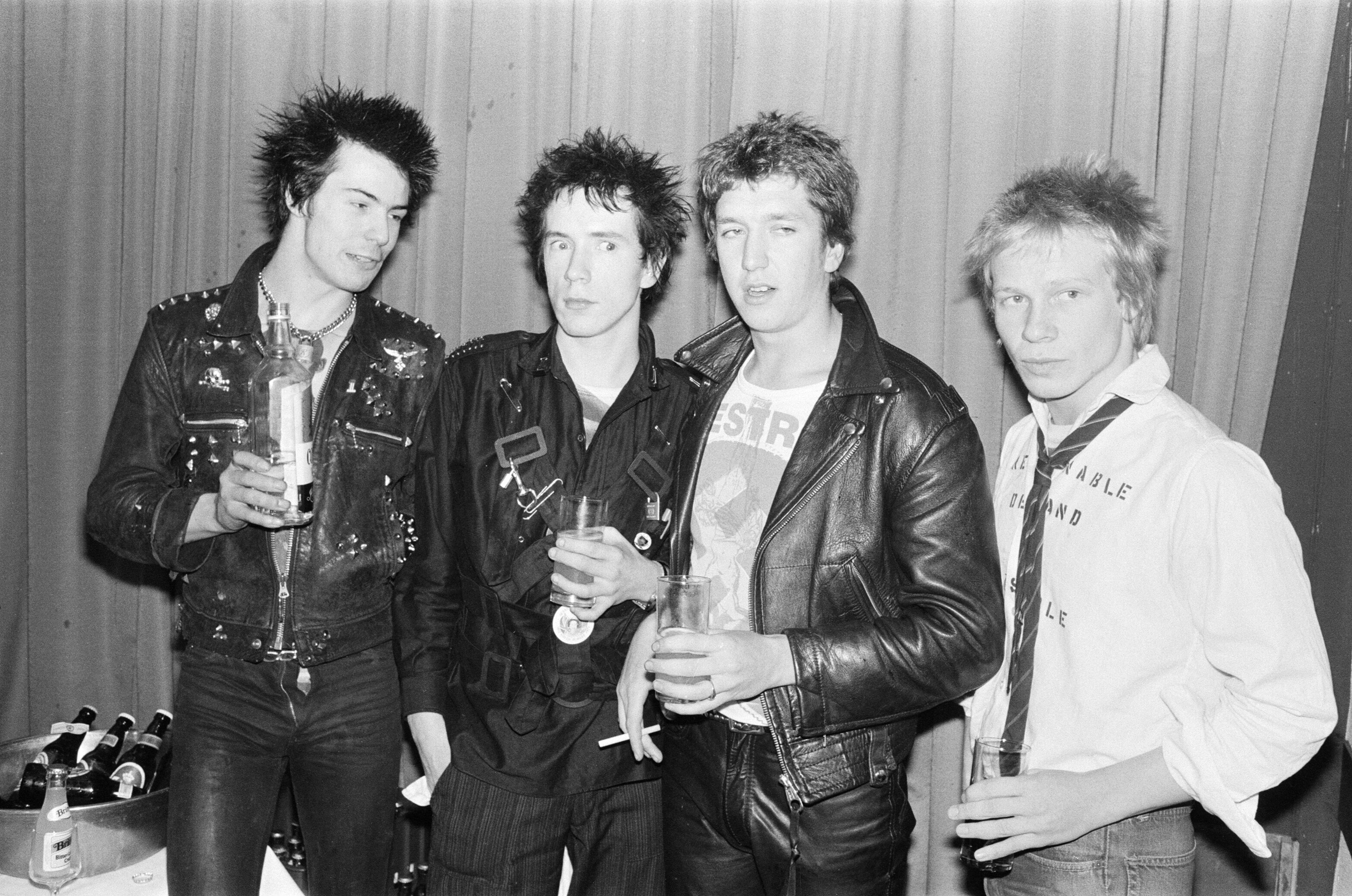 Sid Vicious and the members of the Sex Pistols stand in line in a black-and-white candid photo
