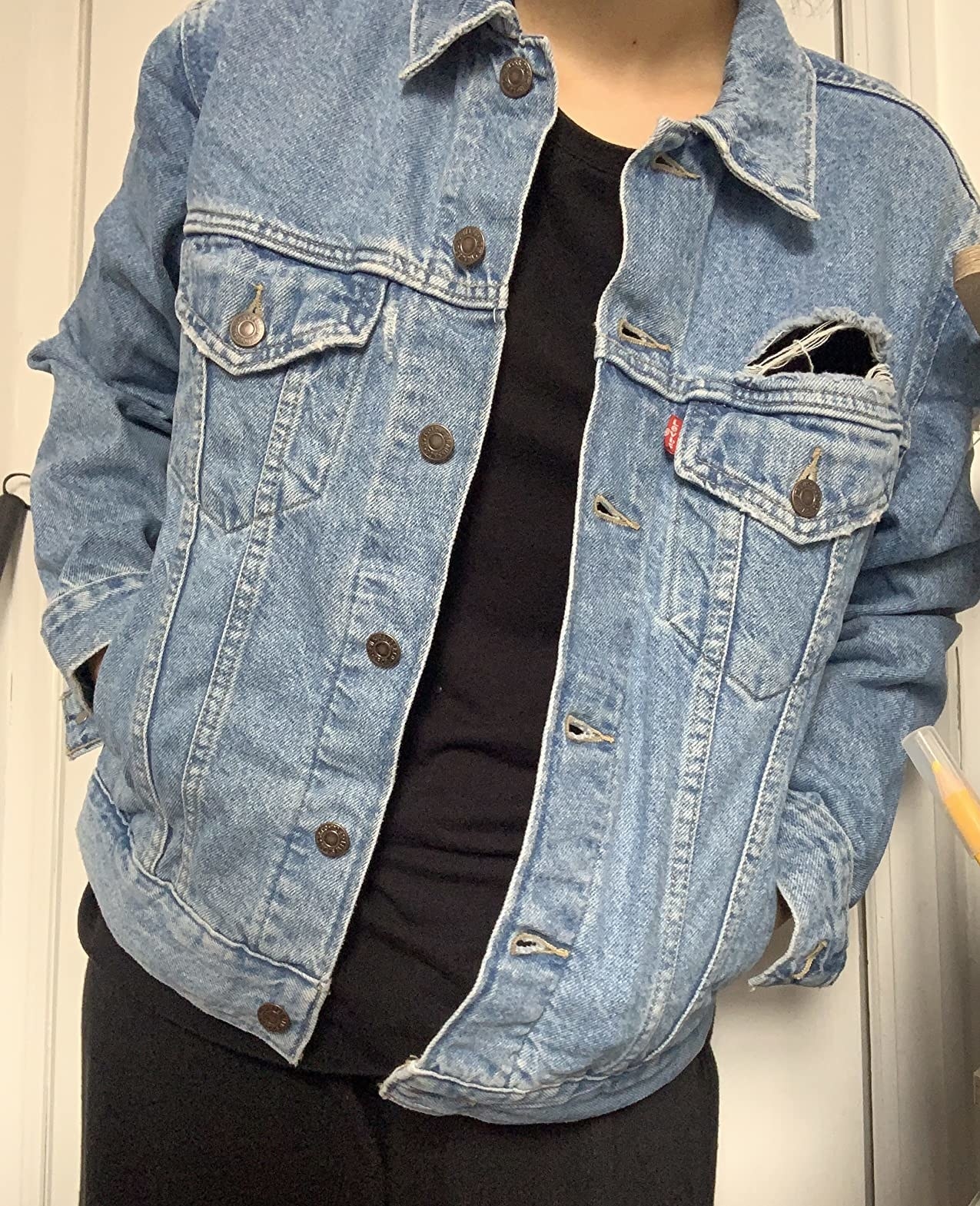 A review wearing an light wash denim jacket with all black outfit