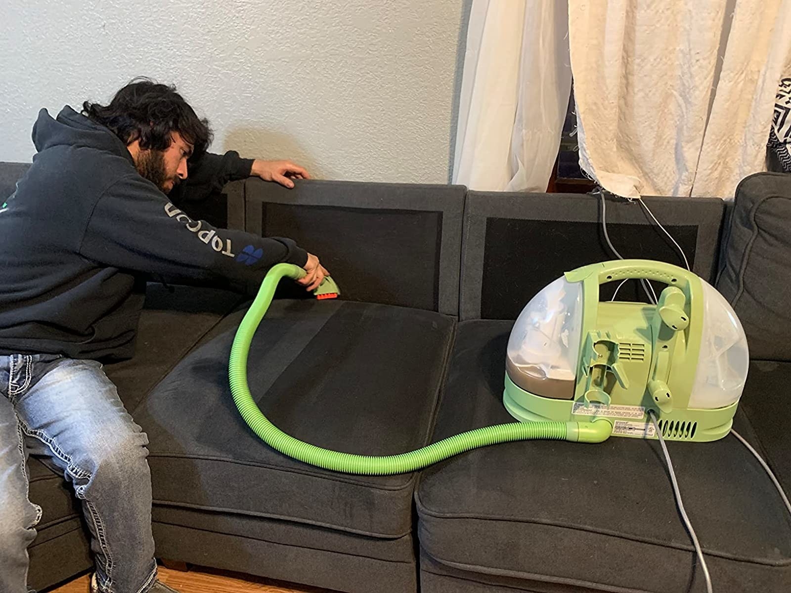 Reviewer using green portable vacuum on dark gray couch