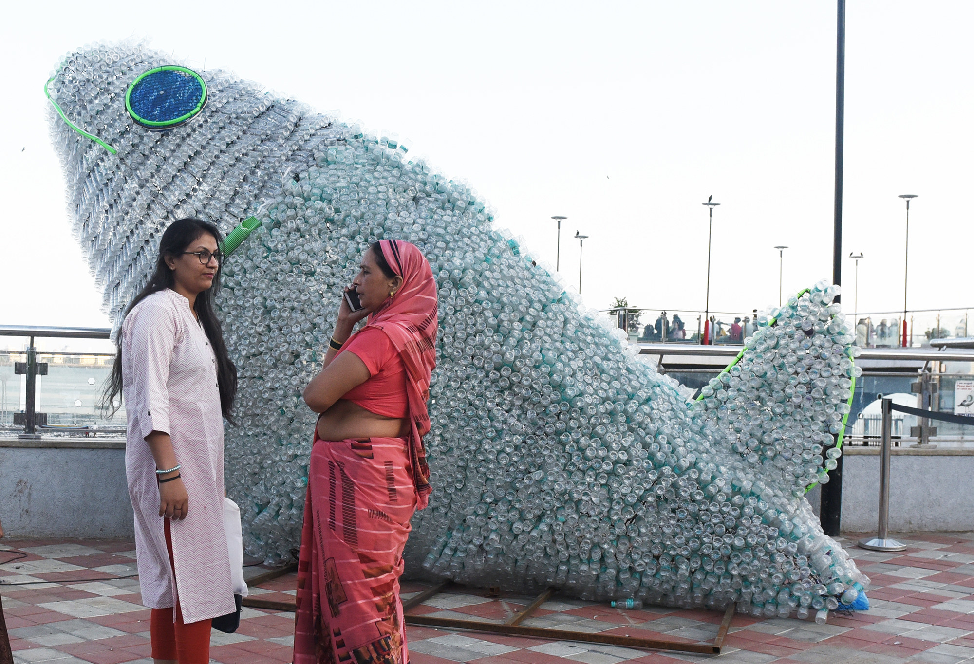two people stand in front of a gigantic whale made out of 6,000 plastic bottles