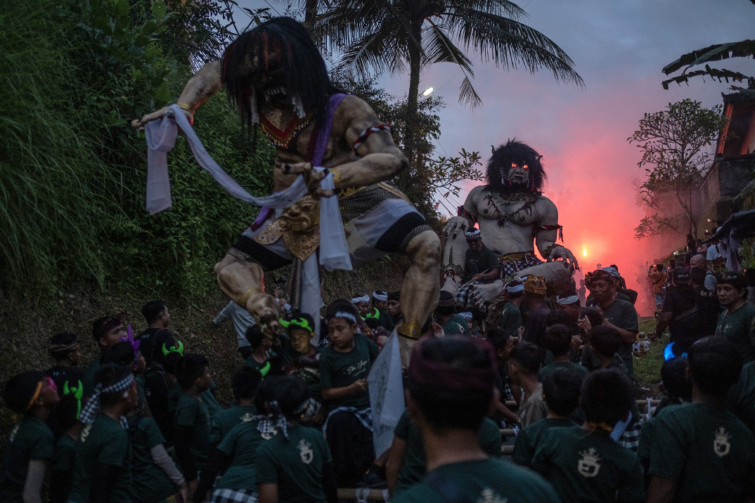 at sunset, a pack of children carry two gigantic demon effiges