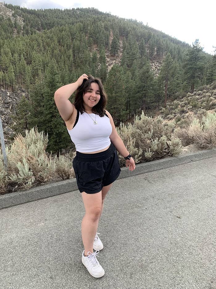 Reviewer standing in front of hilly landscape wearing white tank with bralette underneath