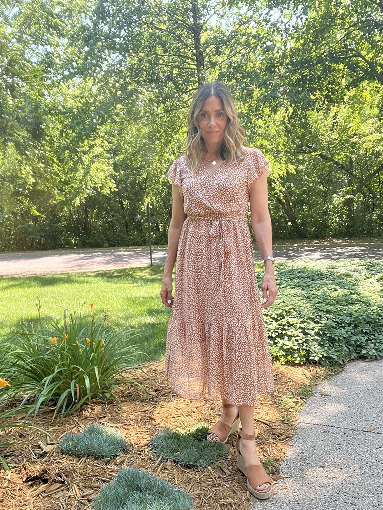 Reviewer standing in front of garden patch in the brown polka dot dress with wedge sandals