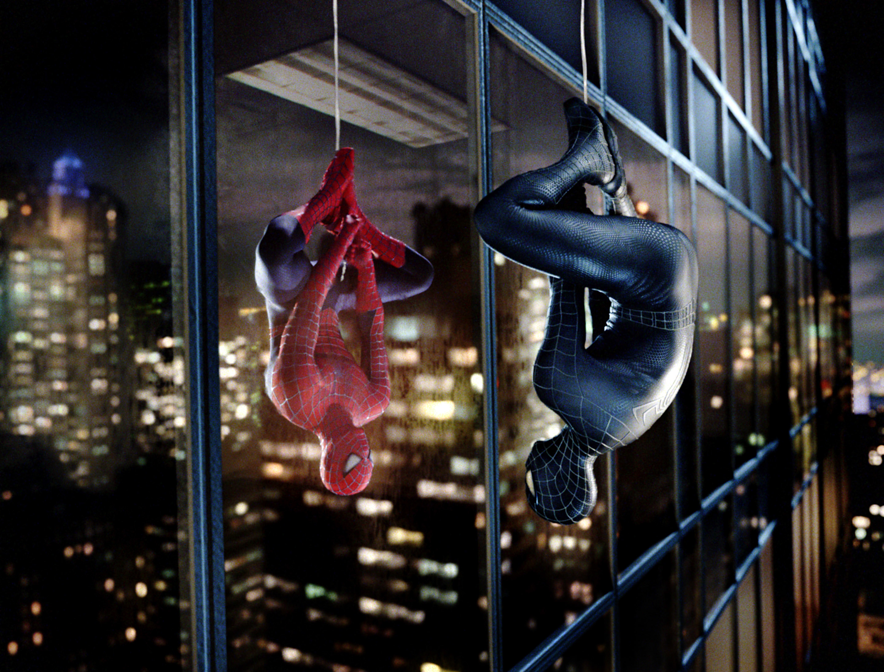 Spider-Man in an all black version of his suit hangs upside down from a building with his reflection showing the traditional red version of the suit