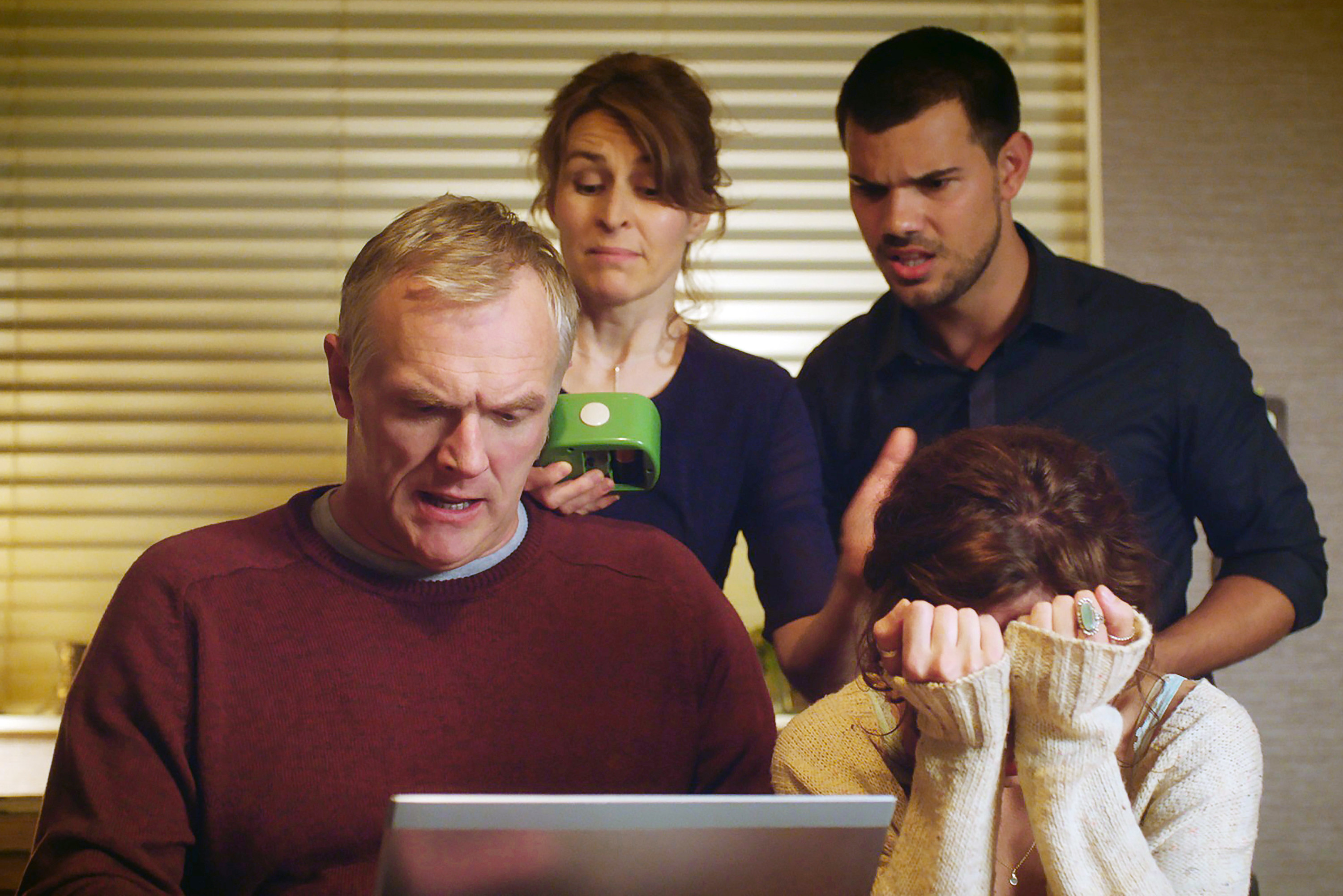 A group of people stand around a laptop, looking disappointed