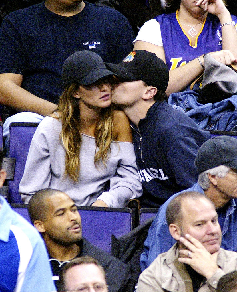 They&#x27;re in the stands of a sports event, both wearing caps, and she looks bored