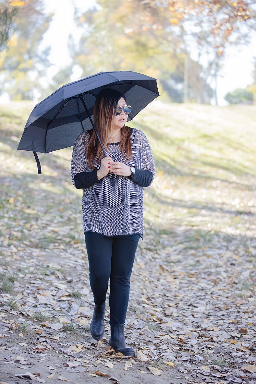 Reviewer standing in fallen leaves with black umbrella open above head