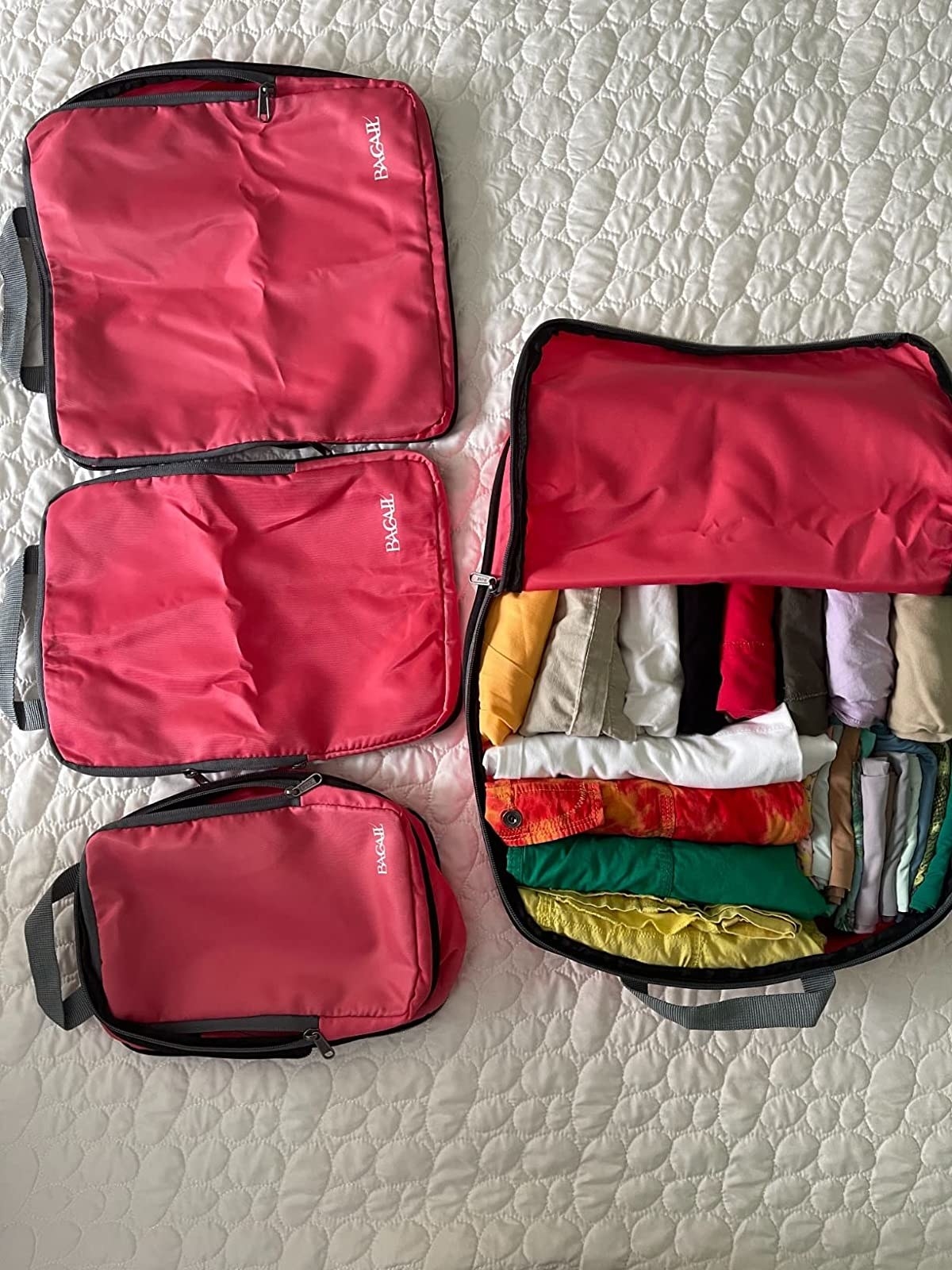 Reviewer&#x27;s packing cubes on bedspread with largest cube filled with neatly folded clothes