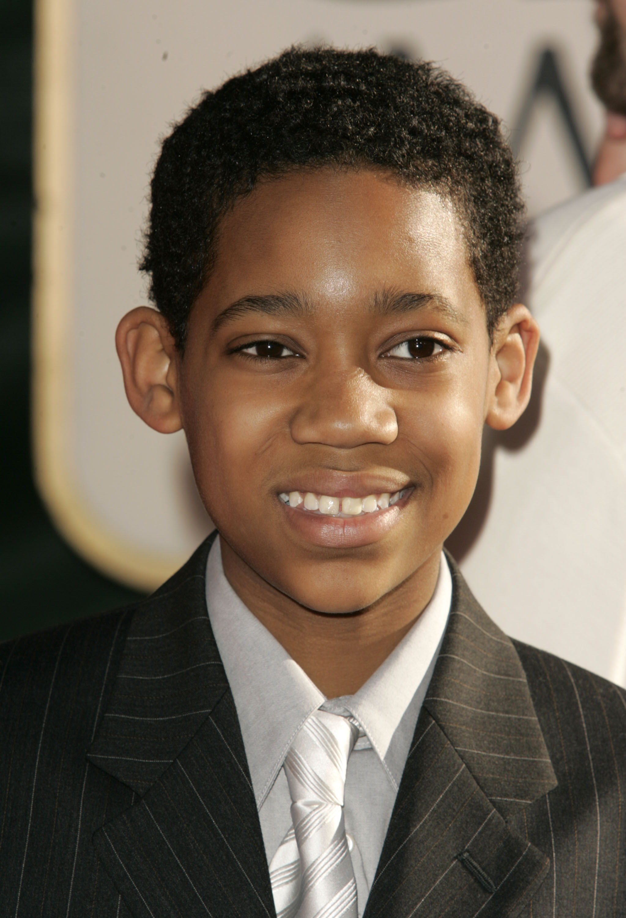 A pre-teen Tyler smiles at a red carpet event. Tyler is wearing a suit and tie