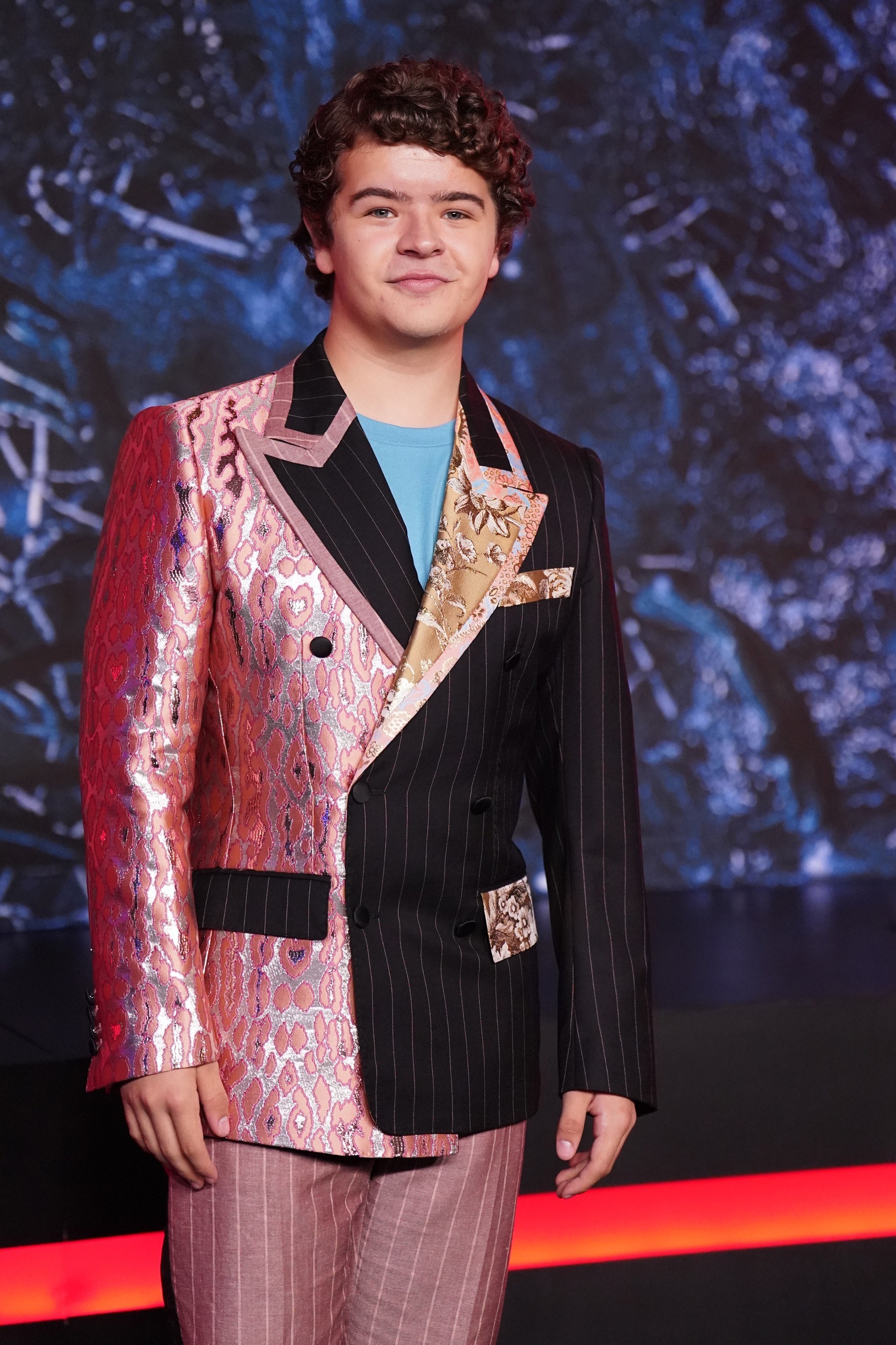 Gaten is wearing a multi-textured, multi-colored suit at a red carpet event