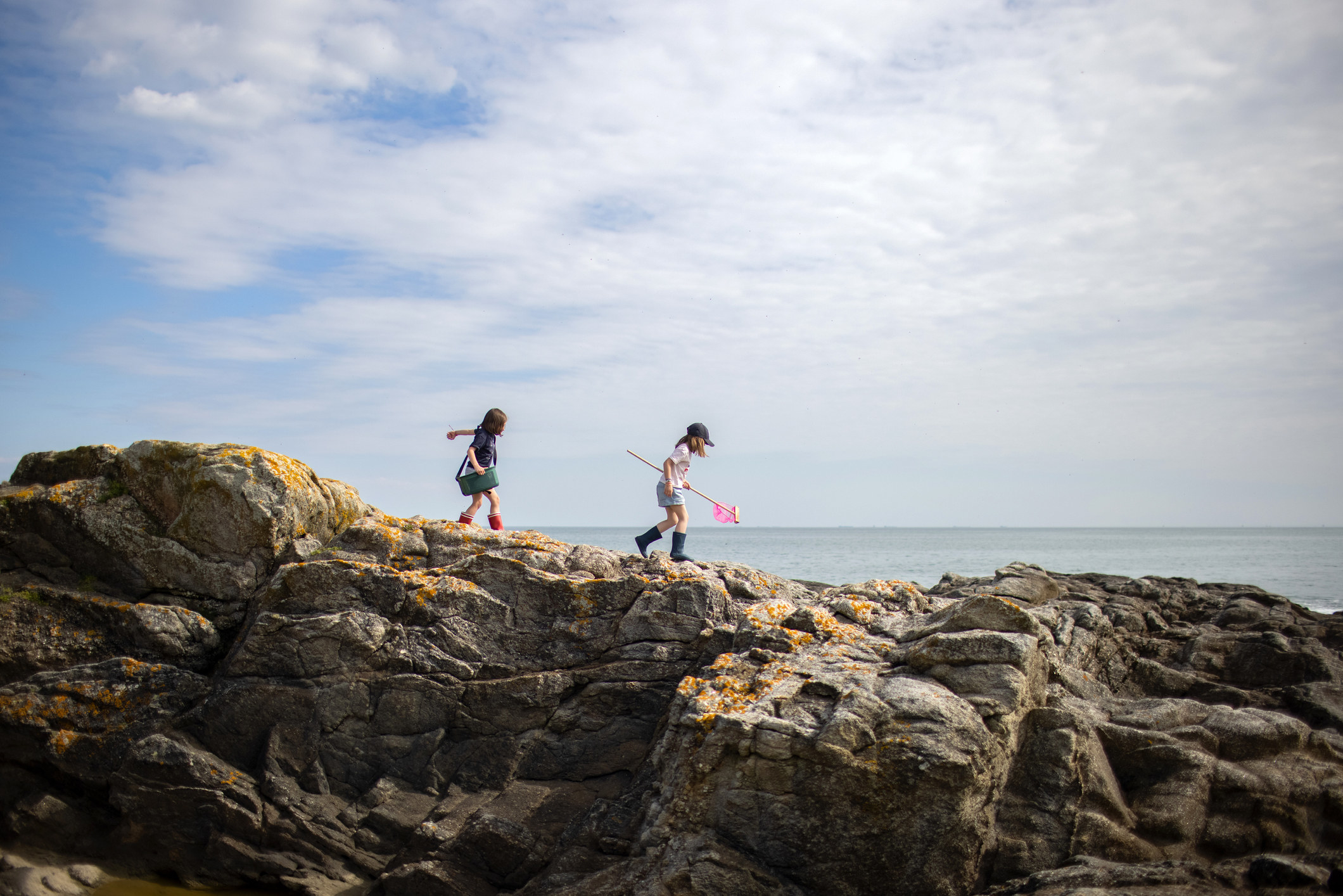Two girls walking on rocks by the seaside.