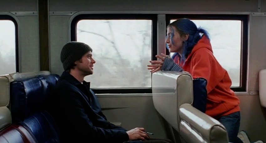 Jim Carrey as Joel sits on a train and Kate Winslet as Clementine sits backwards in the seat in front of him talking to him