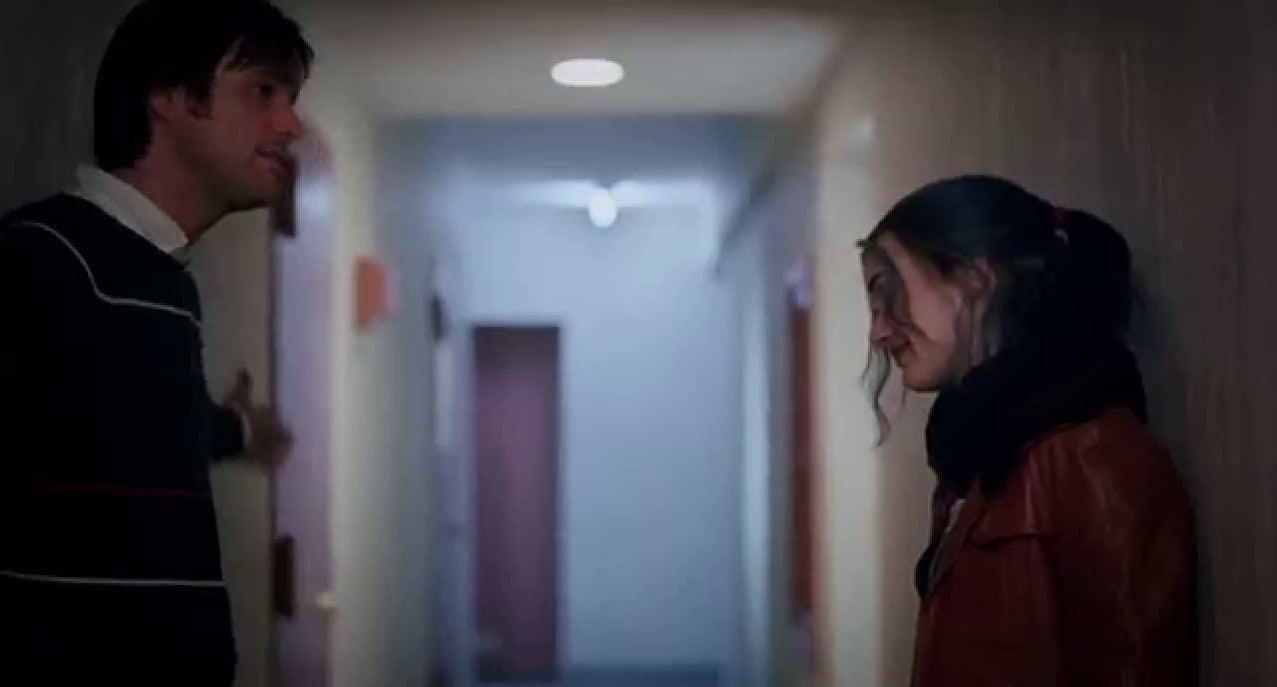 Jim Carrey as Joel and Kate Winslet as Clementine stand across from each other and smile in an apartment building hallway