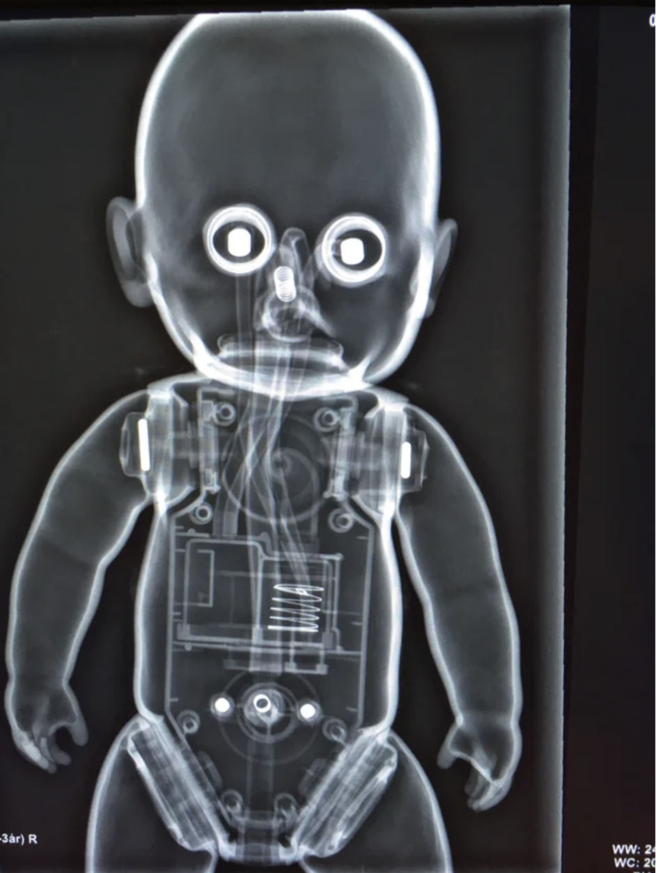 The X-ray image shows the doll's eyes glowing and its mechanical innards are visible through its outer skin