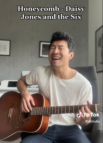 Simu Liu strums his guitar and sings passionately