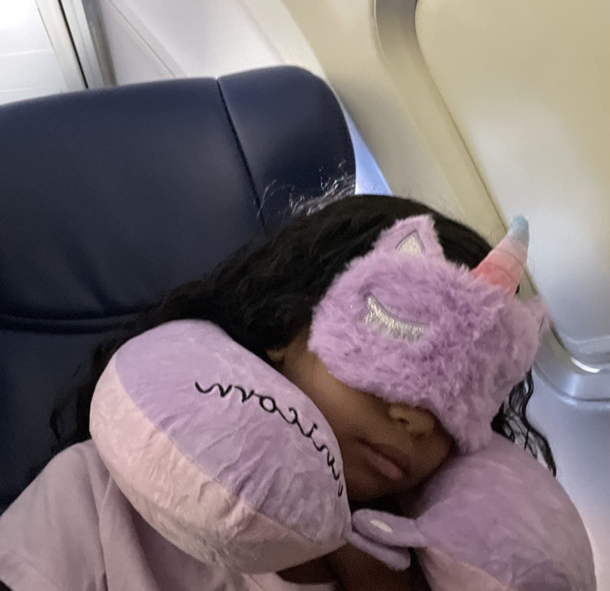 a child sleeping with the pink unicorn-themed neck pillow and mask on plane