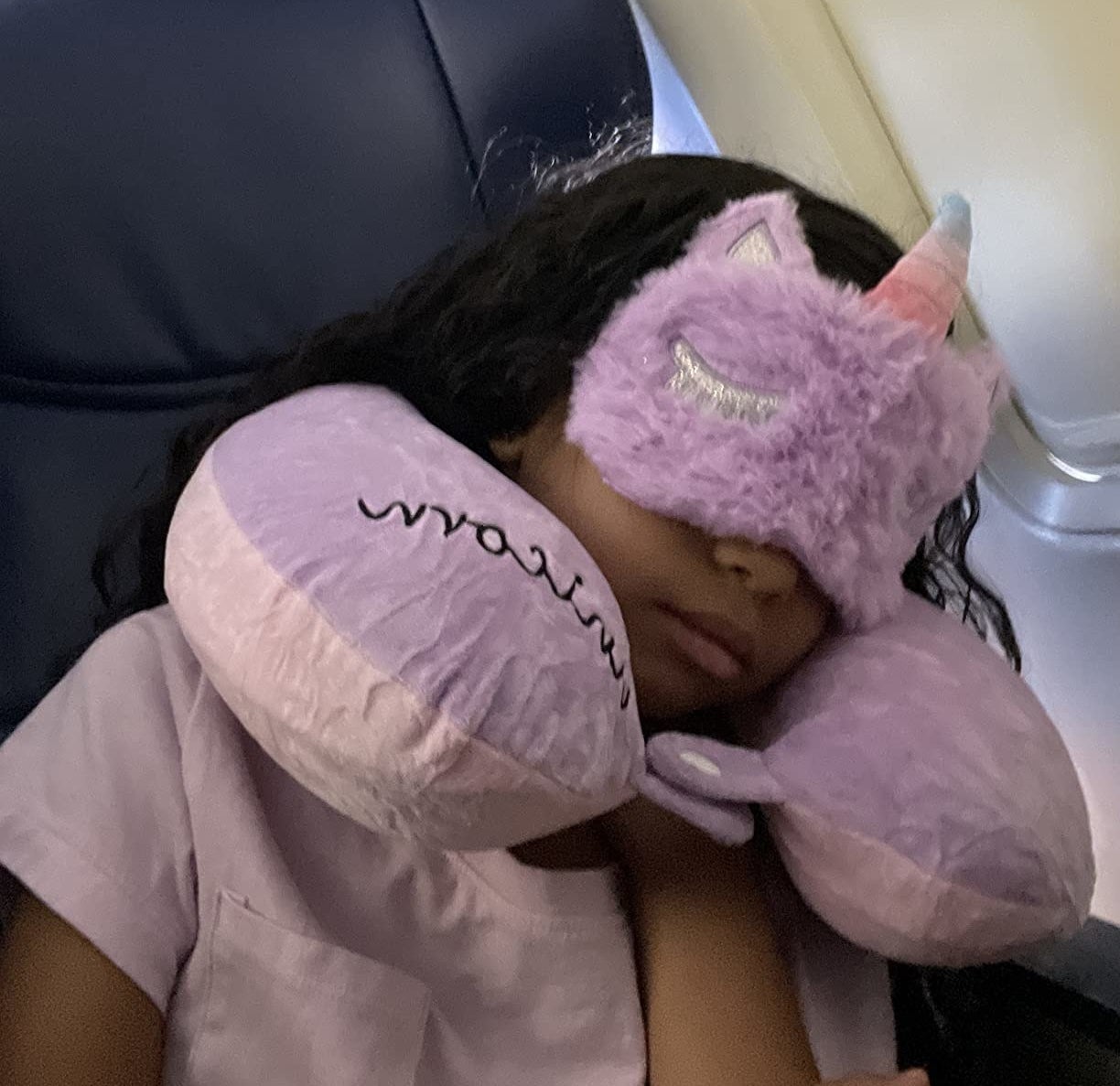 a child sleeping with the pink unicorn-themed neck pillow and mask on plane