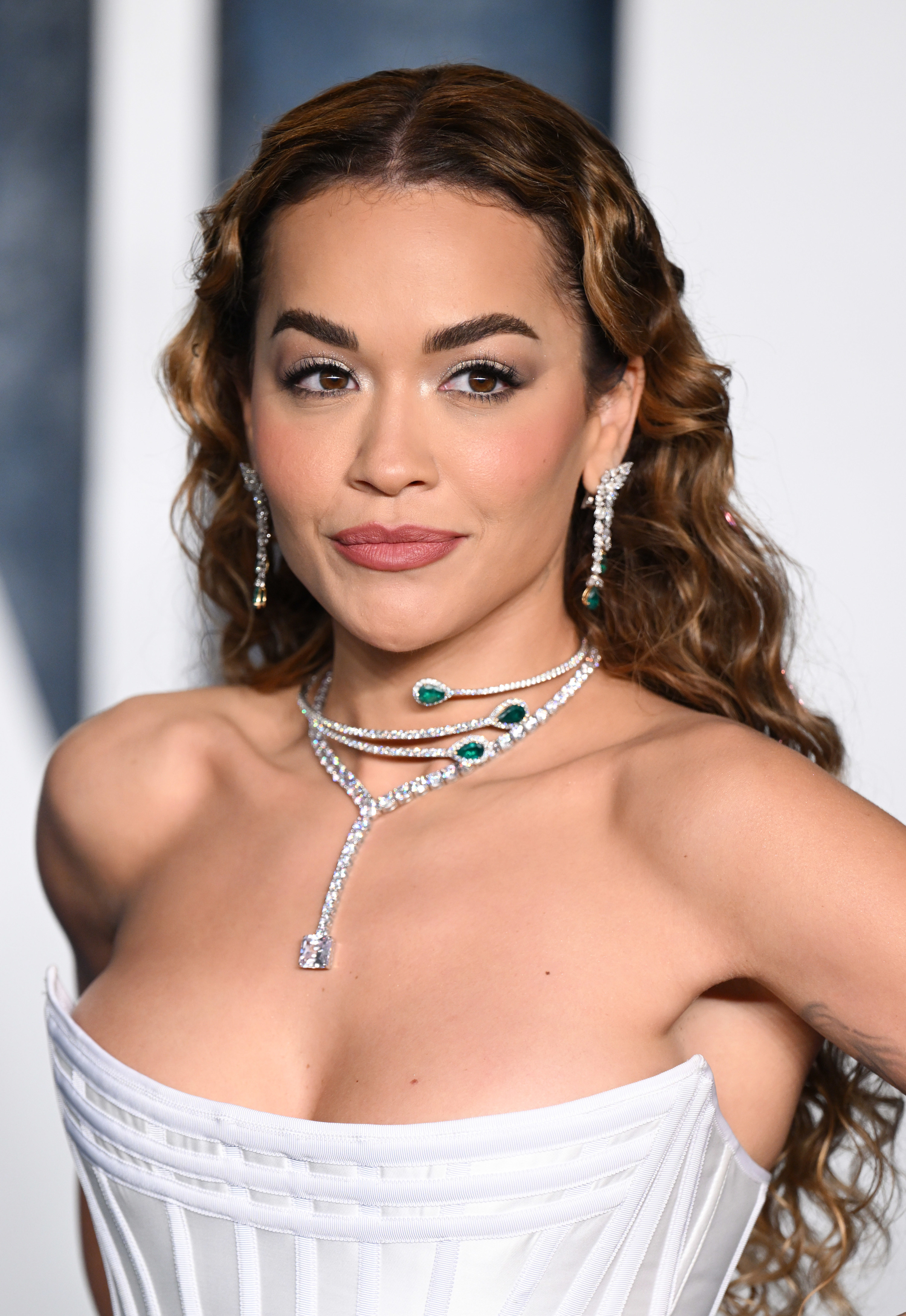 Rita Ora attends the 2023 Vanity Fair Oscar Party. Rita is wearing a strapless dress with a scooped neckline and a diamond and emerald necklace