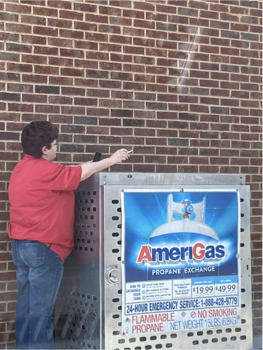 Person flicking their lit cigarette on top of an &quot;AmeriGas propane exchange&quot; machine marked &quot;Flammable&quot; and &quot;No Smoking&quot;