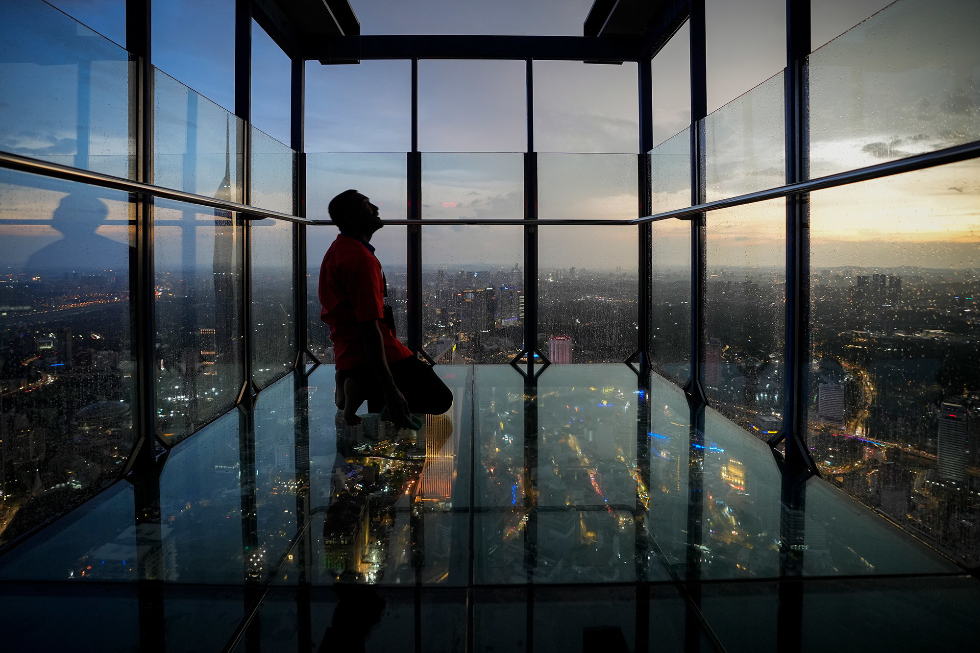 a man kneels in a glass skyscraper at dusk