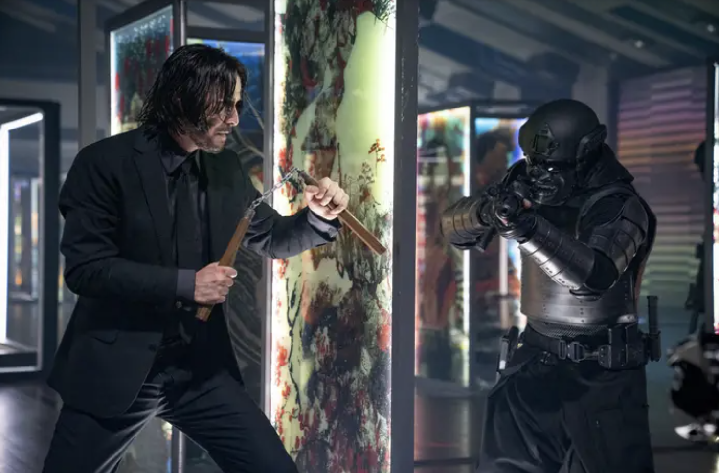 John Wick holds nunchucks and faces a masked armed man in all black