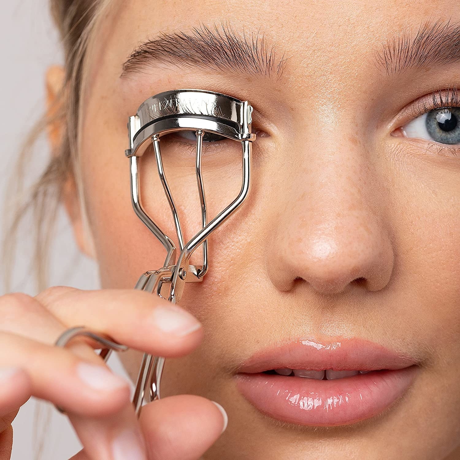 A person curling their eyelashes with an eyelash curler