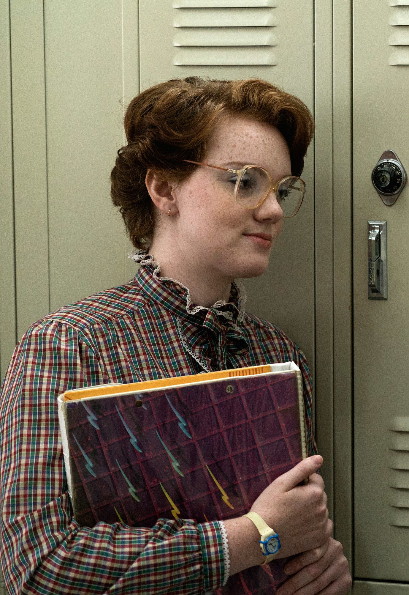 Close-up of Shannon as Barbara from Stranger Things standing next to a school locker