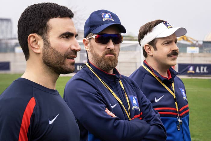 From left to right: Roy Kent, Coach Beard, and Ted Lasso standing by a football pitch