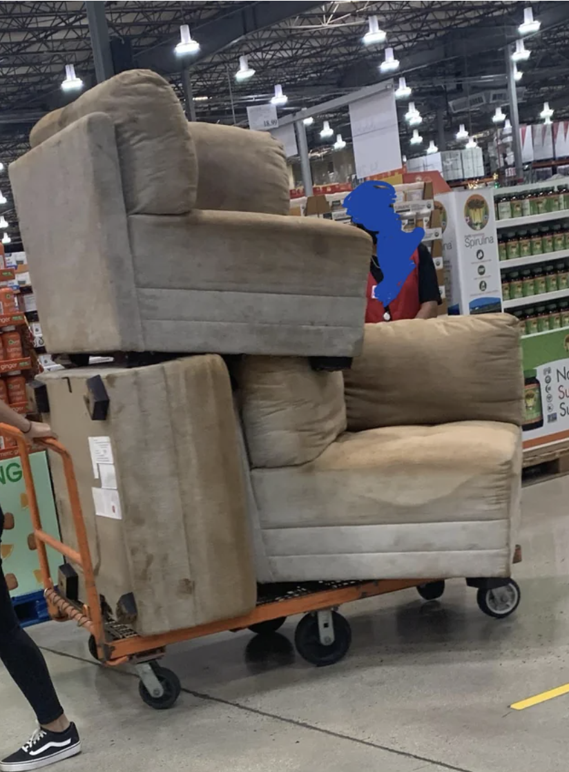 A person pulling a cart with three huge, soiled pieces of a sectional