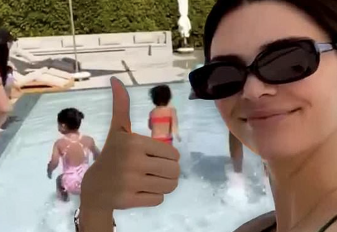 Kendall Jenner giving a thumbs-up as two kids play in a pool behind her