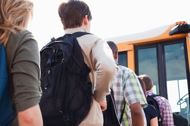 A male student waits in line to get on a school bus