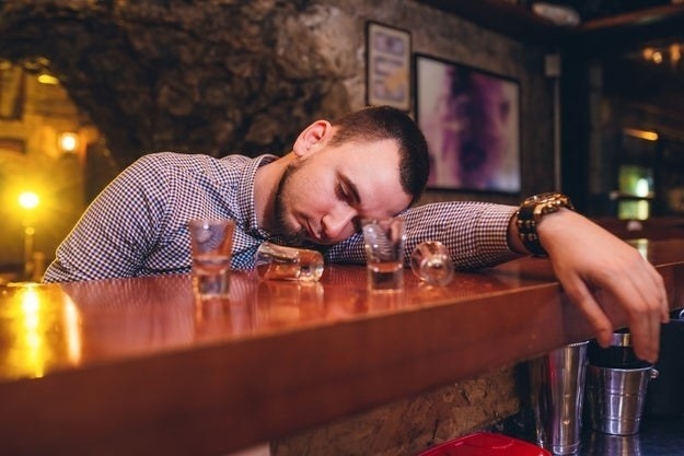 A man passed out drunk at a bar, surrounded by empty shot glasses