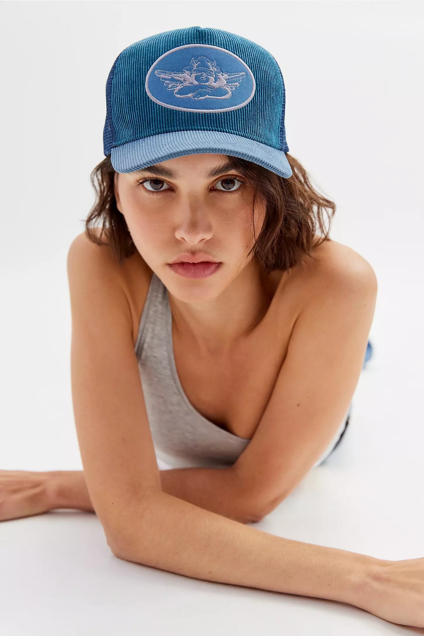 Model wearing blue corduroy trucker hat with angel embroidered patch on front
