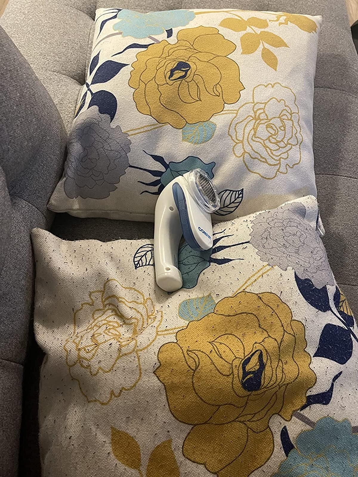 on bottom: floral-print pillow with pilling on front. on top: matching pillow with no pilling after using the lint remover