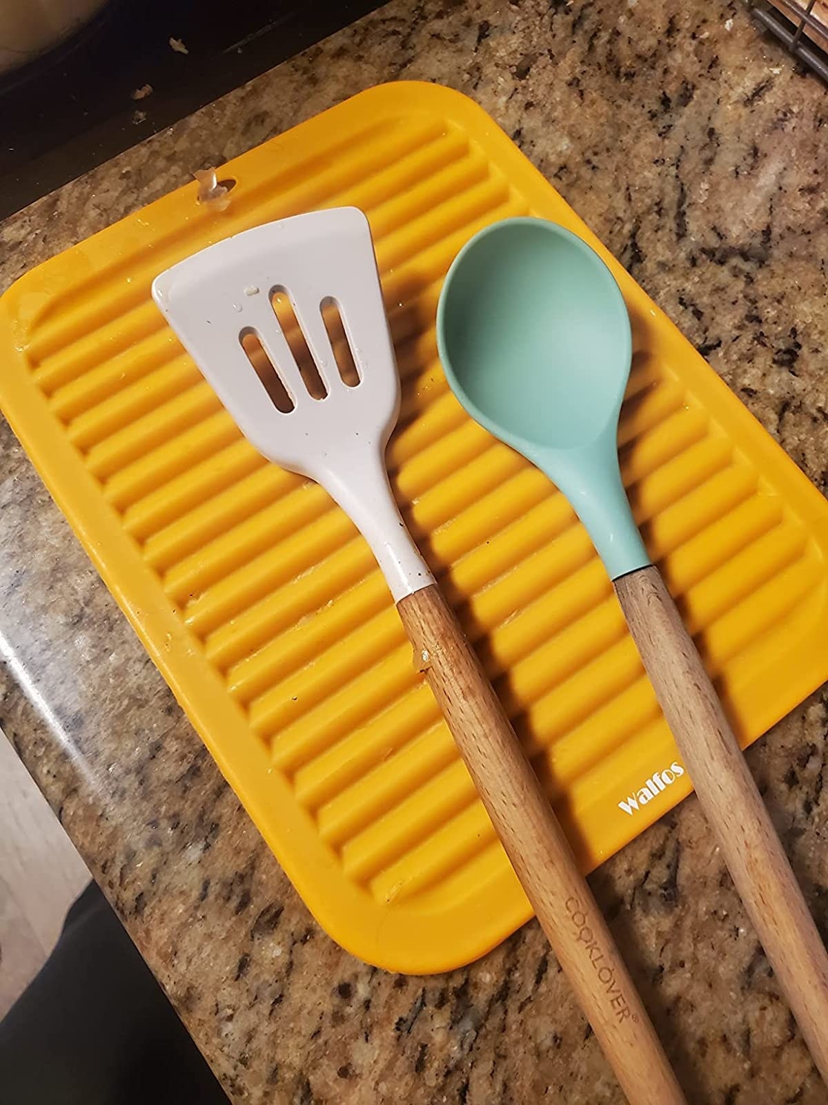 Reviewer image of yellow trivet with cooking utensils on it