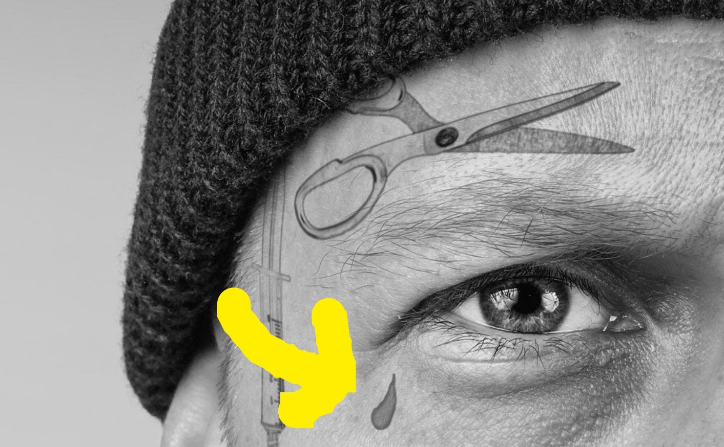 arrow pointing to a filled in tear drop tattoo underneath an eye