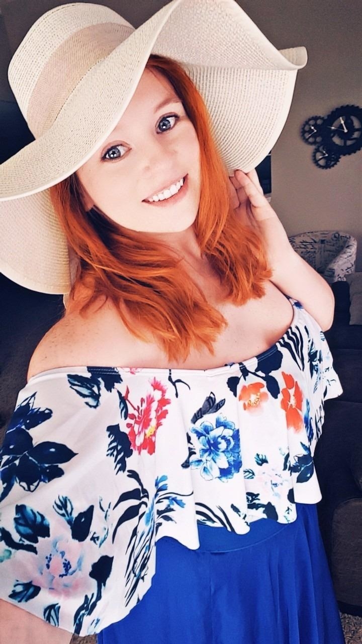 Reviewer wearing beige floppy sunhat with white floral shirt and blue skirt