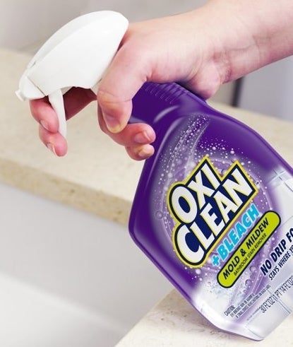 a person spraying a bottle of OxiClean Mold &amp;amp; Mildew remover onto a sink