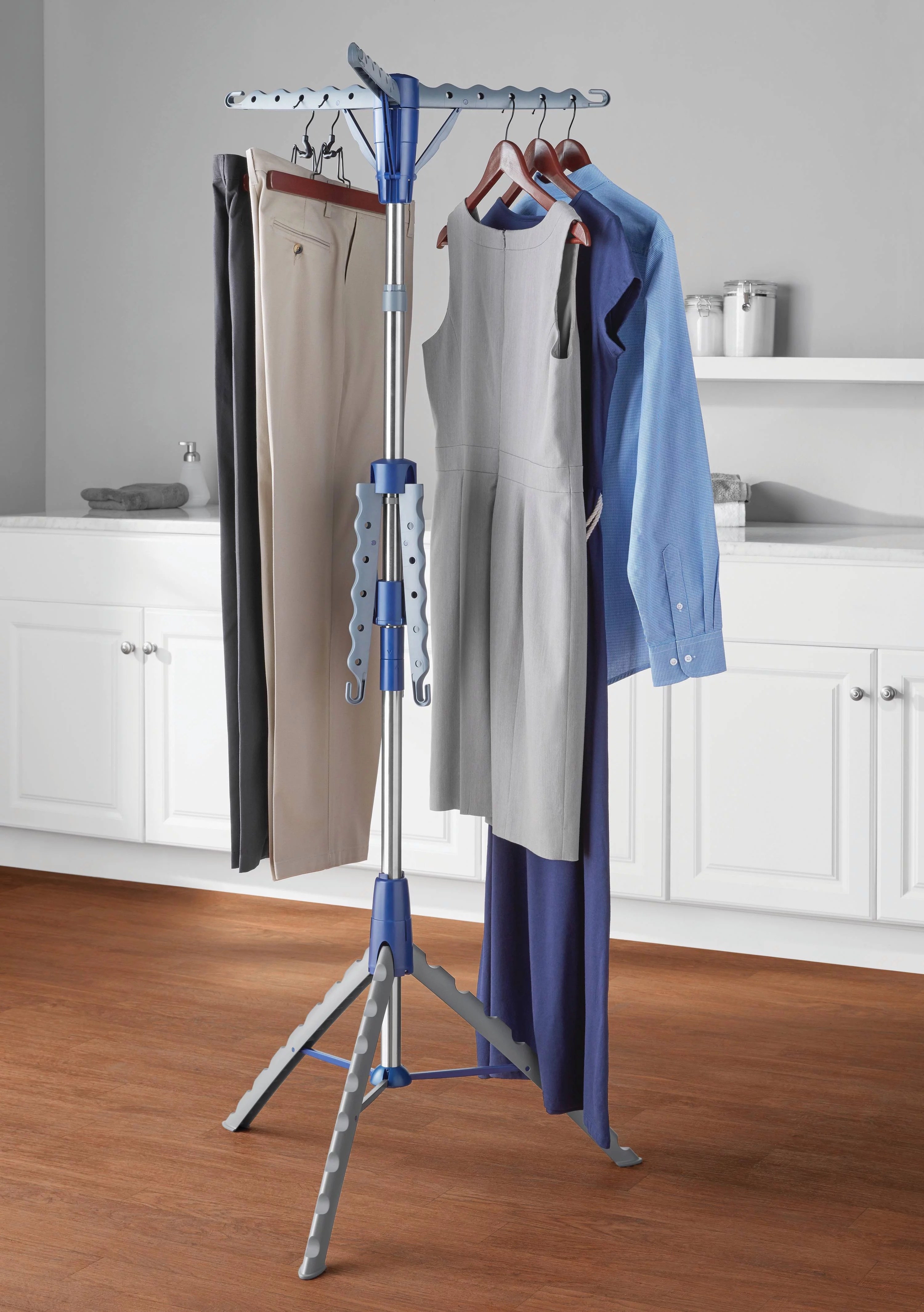 a blue and gray drying rack on a hardwood floor holding plants and dresses