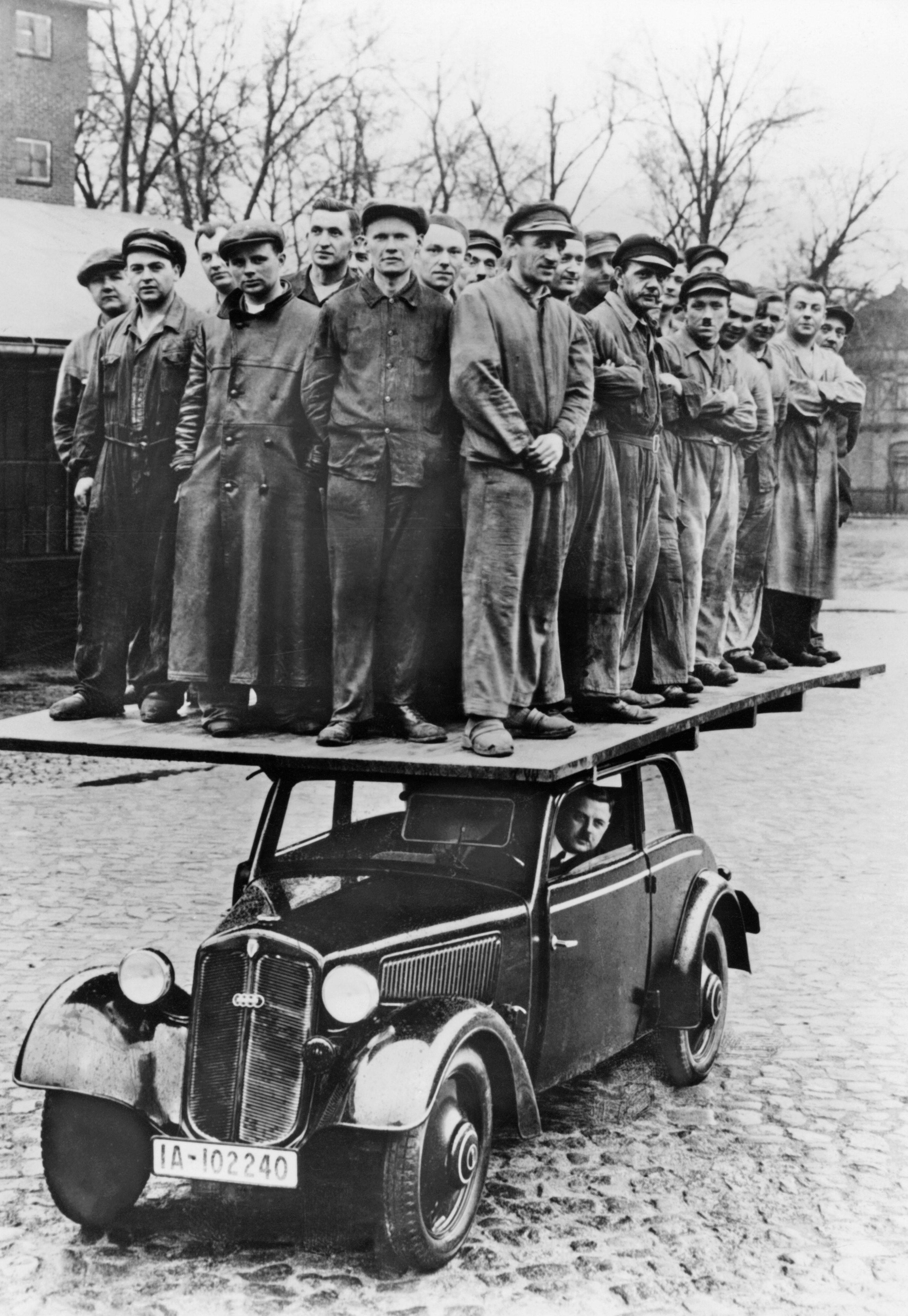 A man at the wheel as what looks like dozens of men stand on a wooden board on the roof