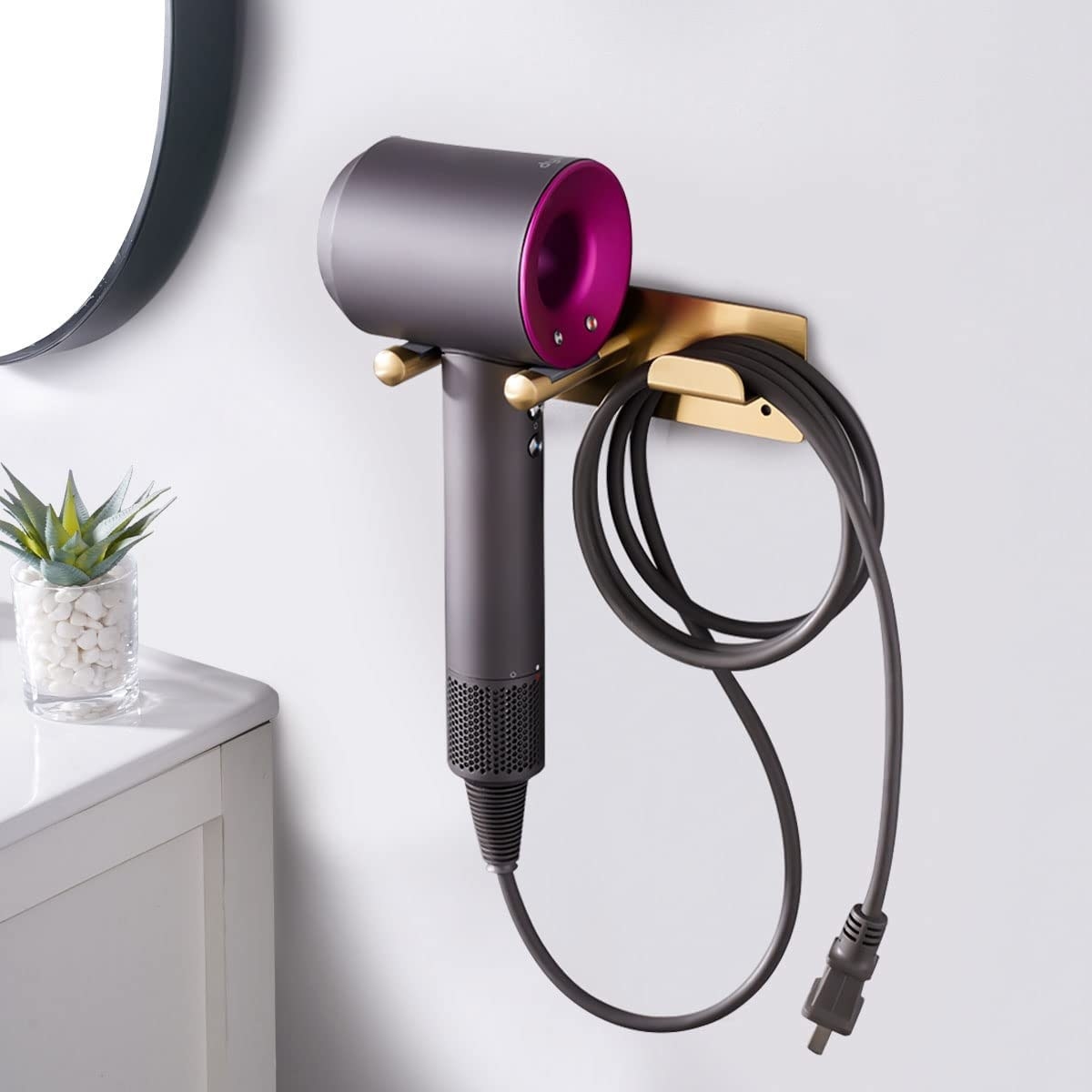Dyson hair dryer with attachments mounted on a wall, a small plant and mirror in the background