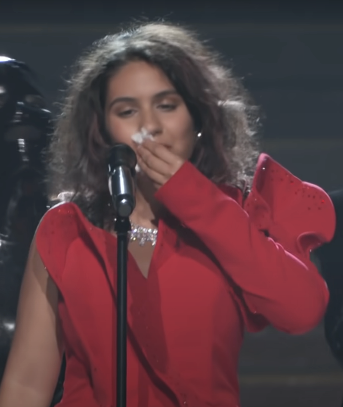 Alessia at a microphone wiping her makeup off with a tissue