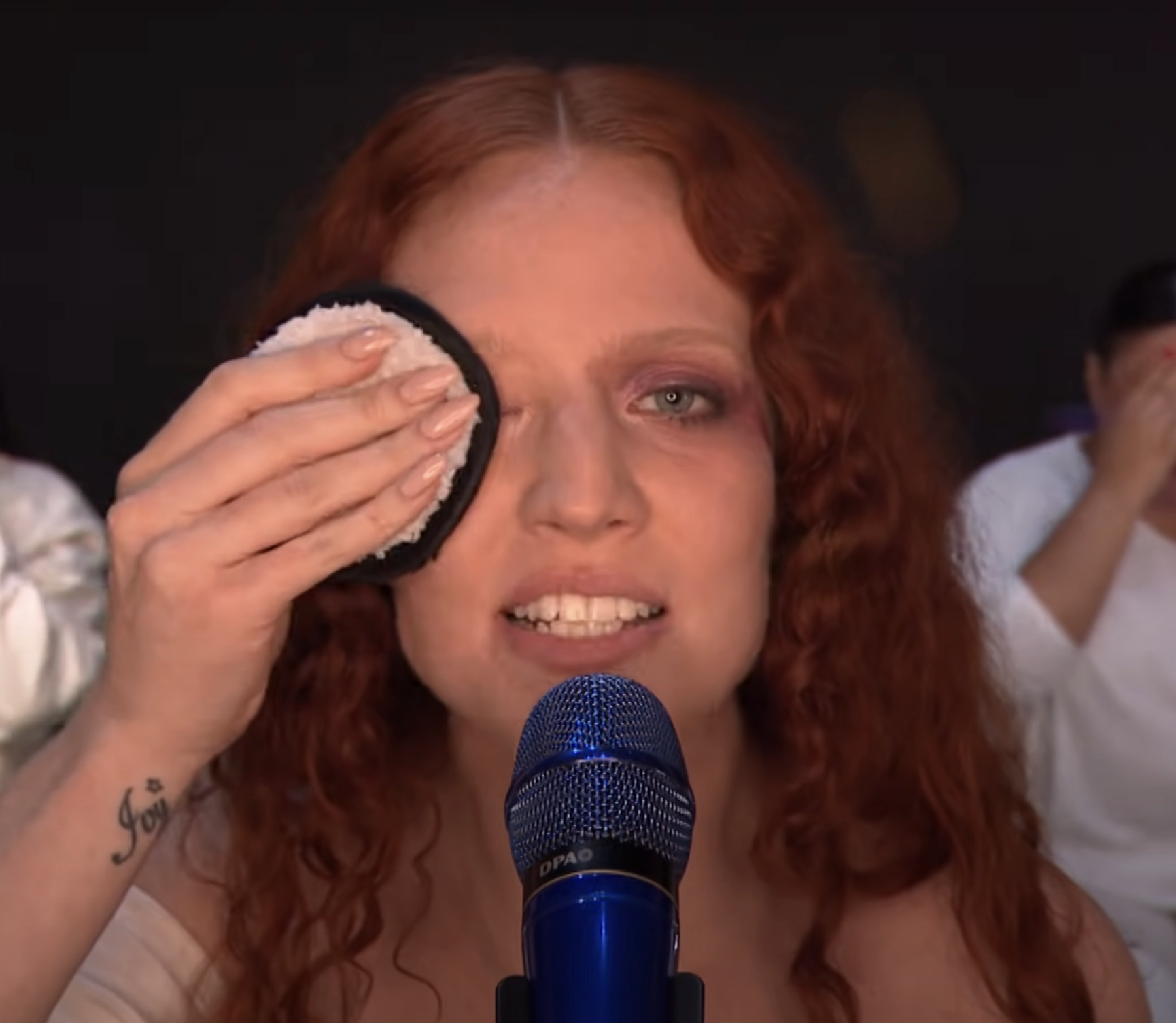 Jess in front of a microphone wiping makeup off her face with a makeup puff
