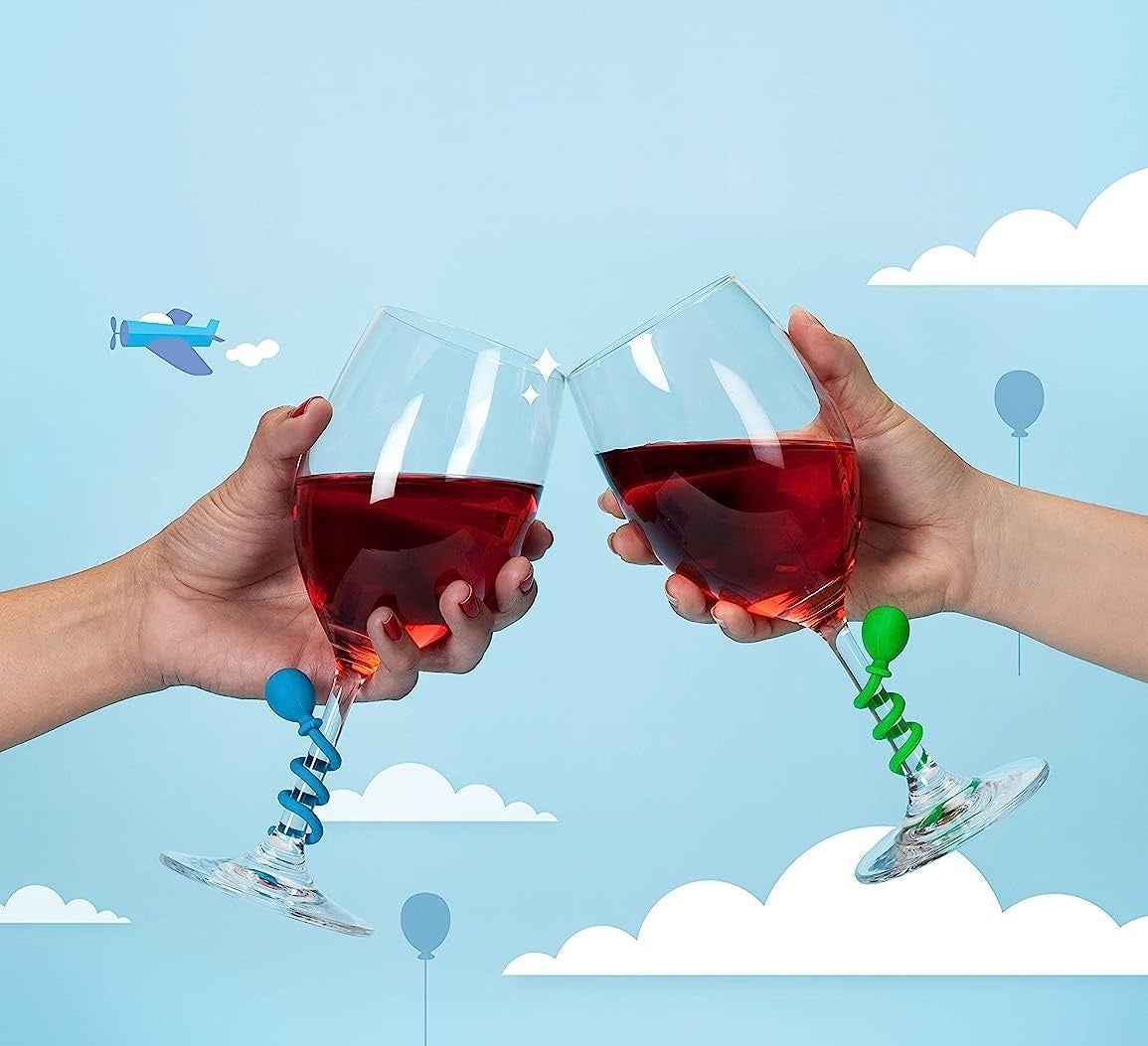 two people clinking their wine glasses together with the drink charms wound around the stem