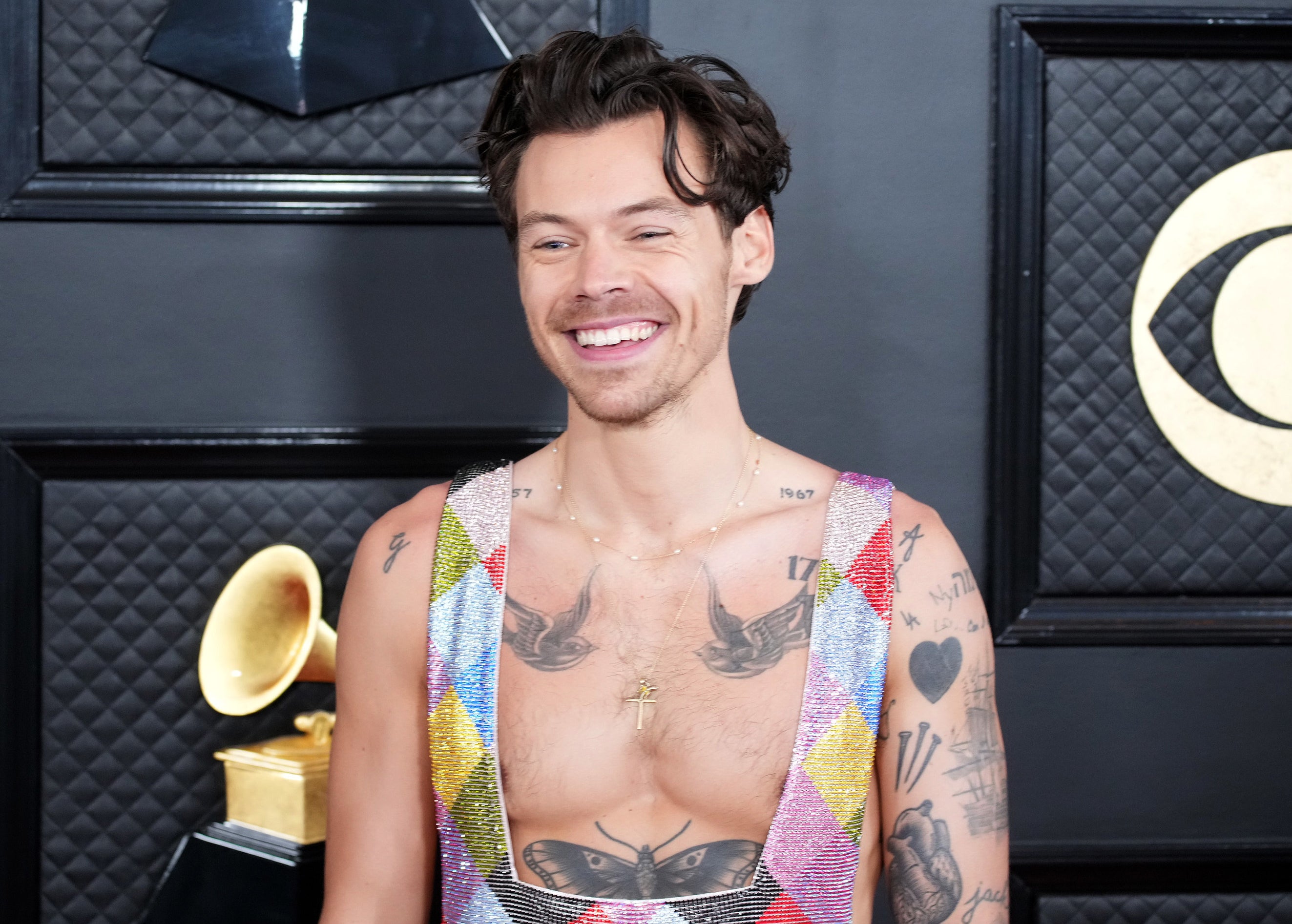 Harry smiling in colorful overalls and bare-chested