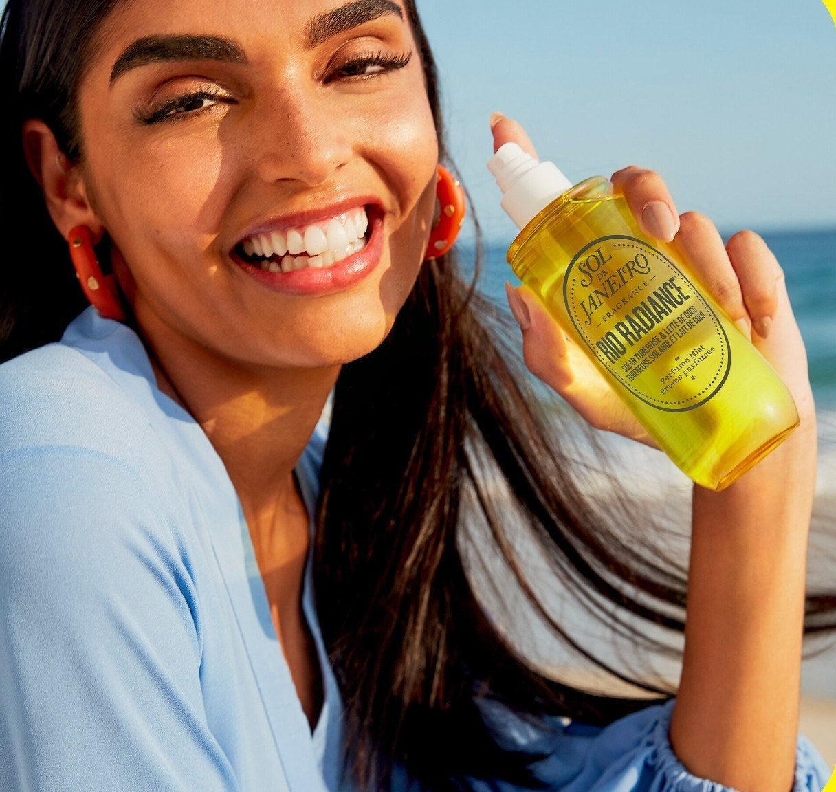 a smiling person holding up a bottle of the sol de janeiro perfume mist