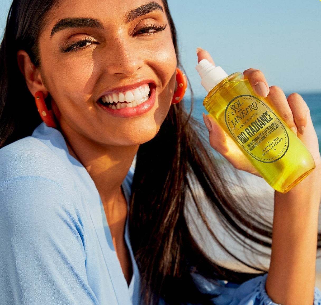 a smiling person holding up a bottle of the sol de janeiro perfume mist