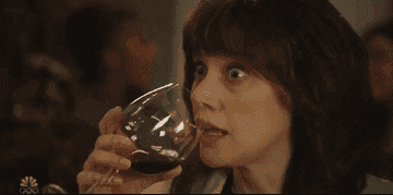 A woman looking uncomfortable and drinking wine