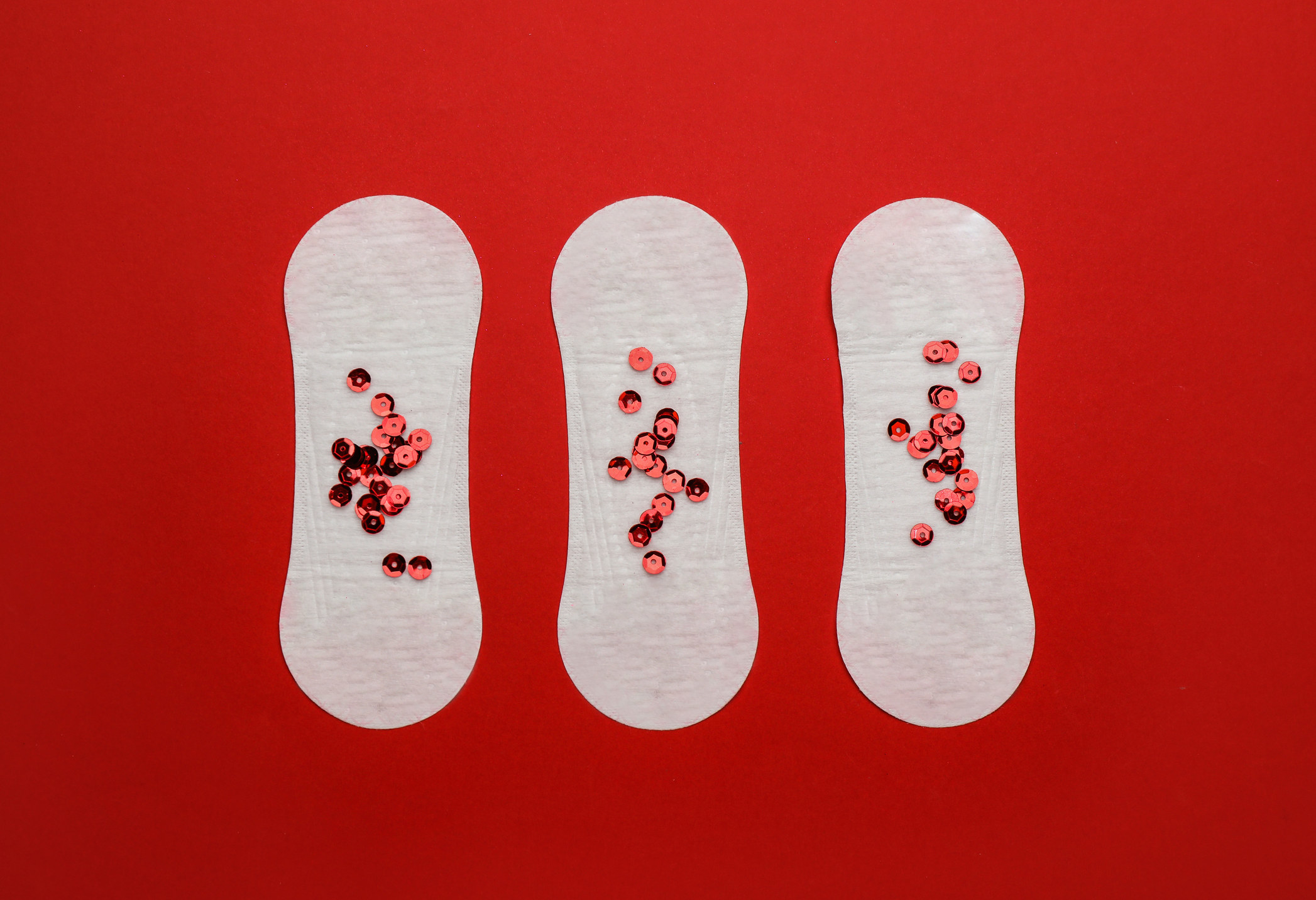 Sanitary pads with sequins on red background, flat lay